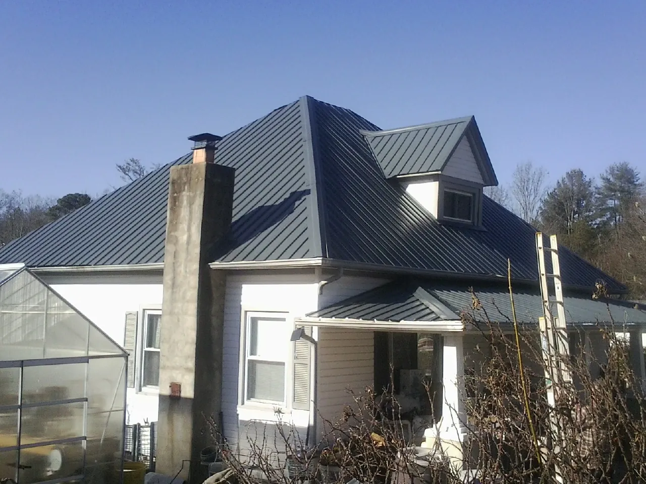 Dark blue standing seam metal roof on a white farmhouse with dormer — Slate & Tile Roof Repair by Roofing Brothers in Kearney