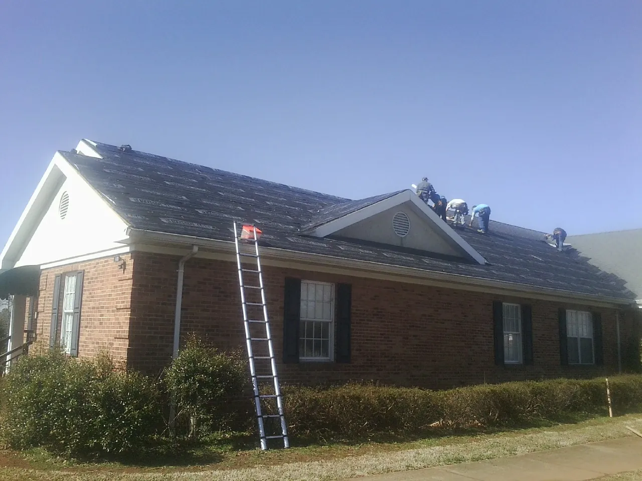 Crew tearing shingles off a brick ranch roof with a ladder set — Emergency Roof Repair work by our crew in Kearney