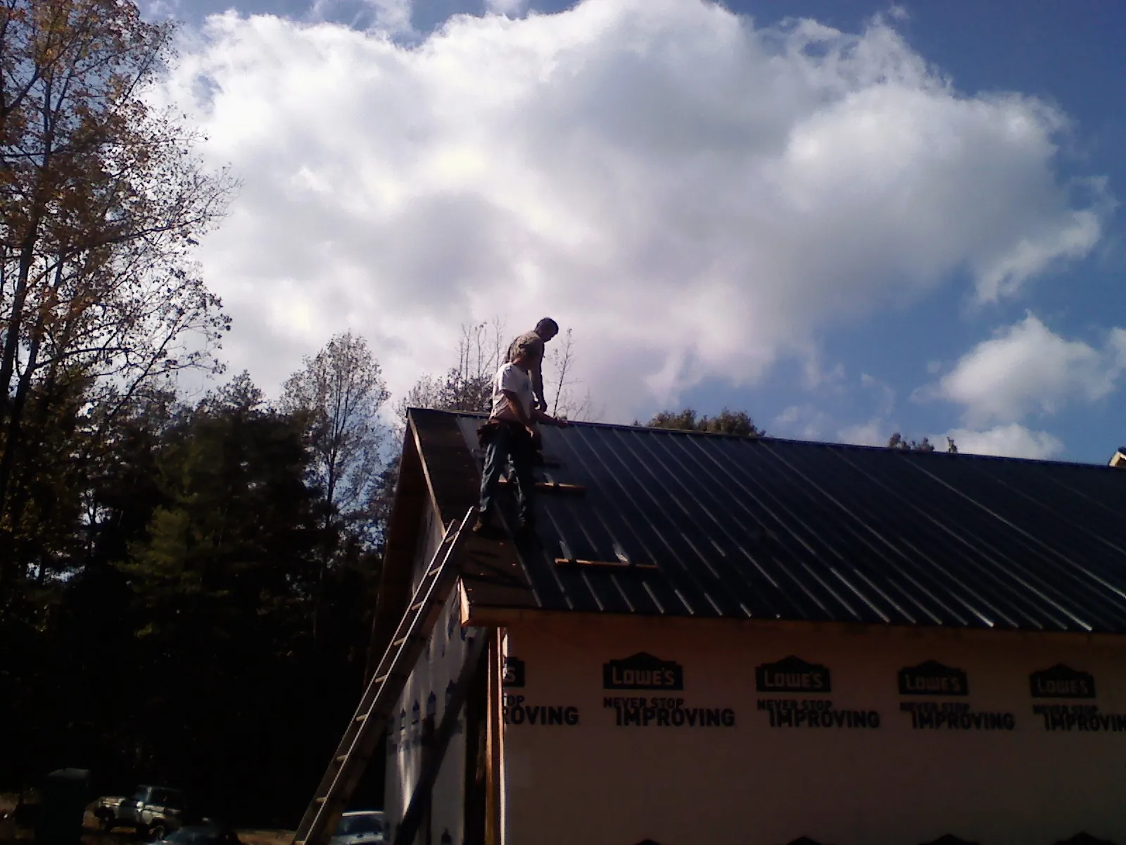 Roofer fastening dark metal panels high against a cloudy sky, from a Roof Inspection job in Kearney